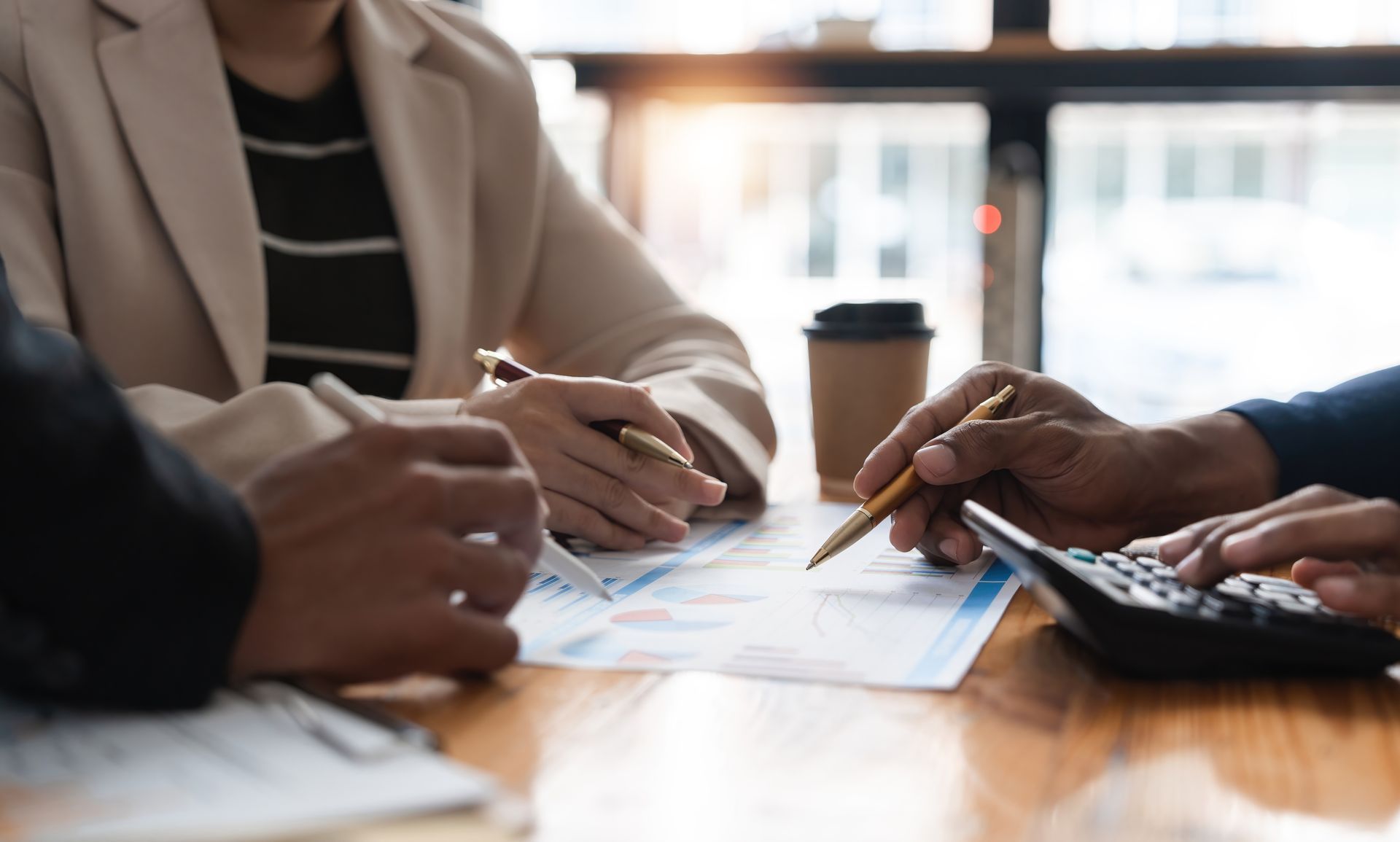 Hands reviewing documents at a meeting table with coffee and a calculator