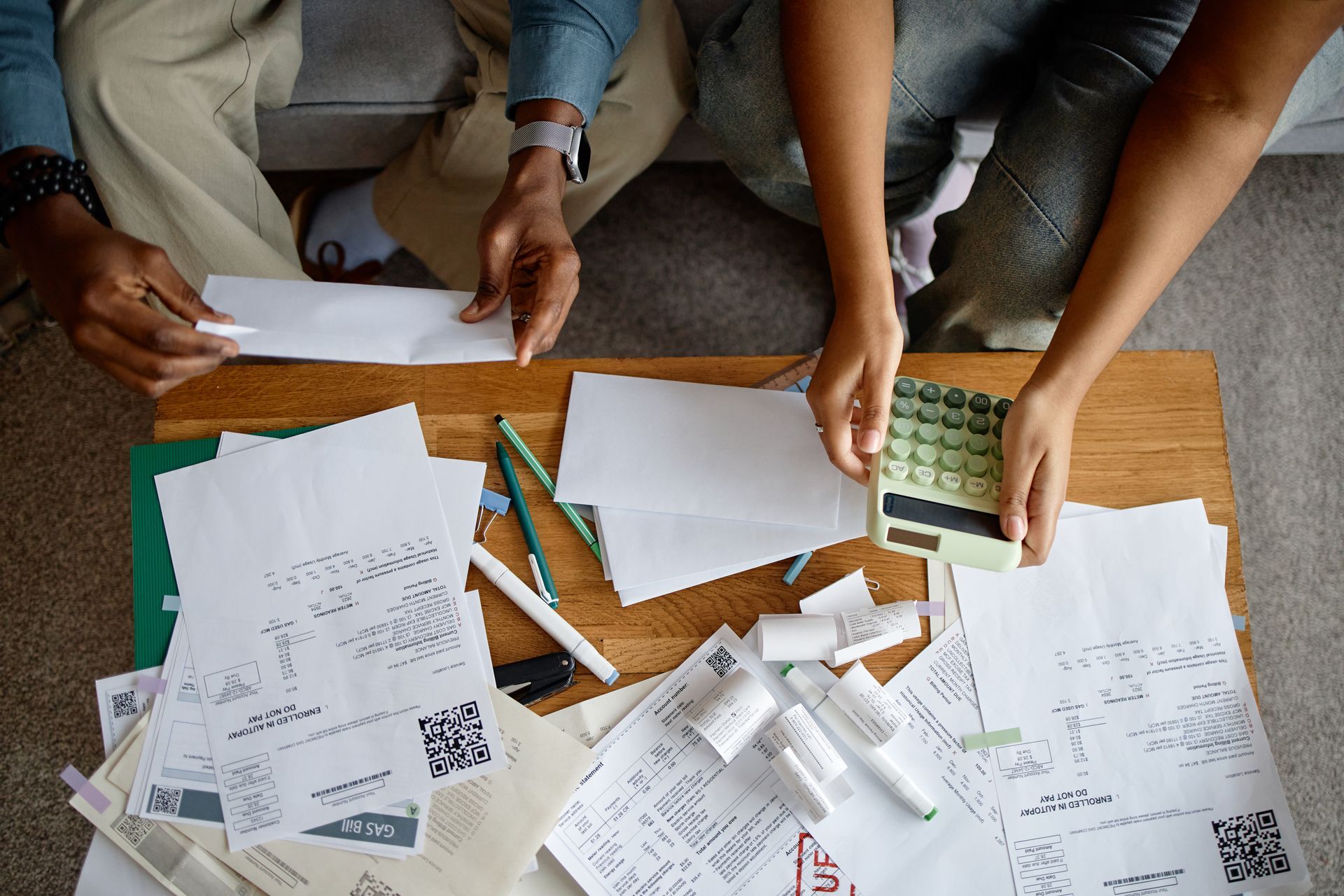 Hands working over paperwork and receipts on a wooden table with a calculator and pens