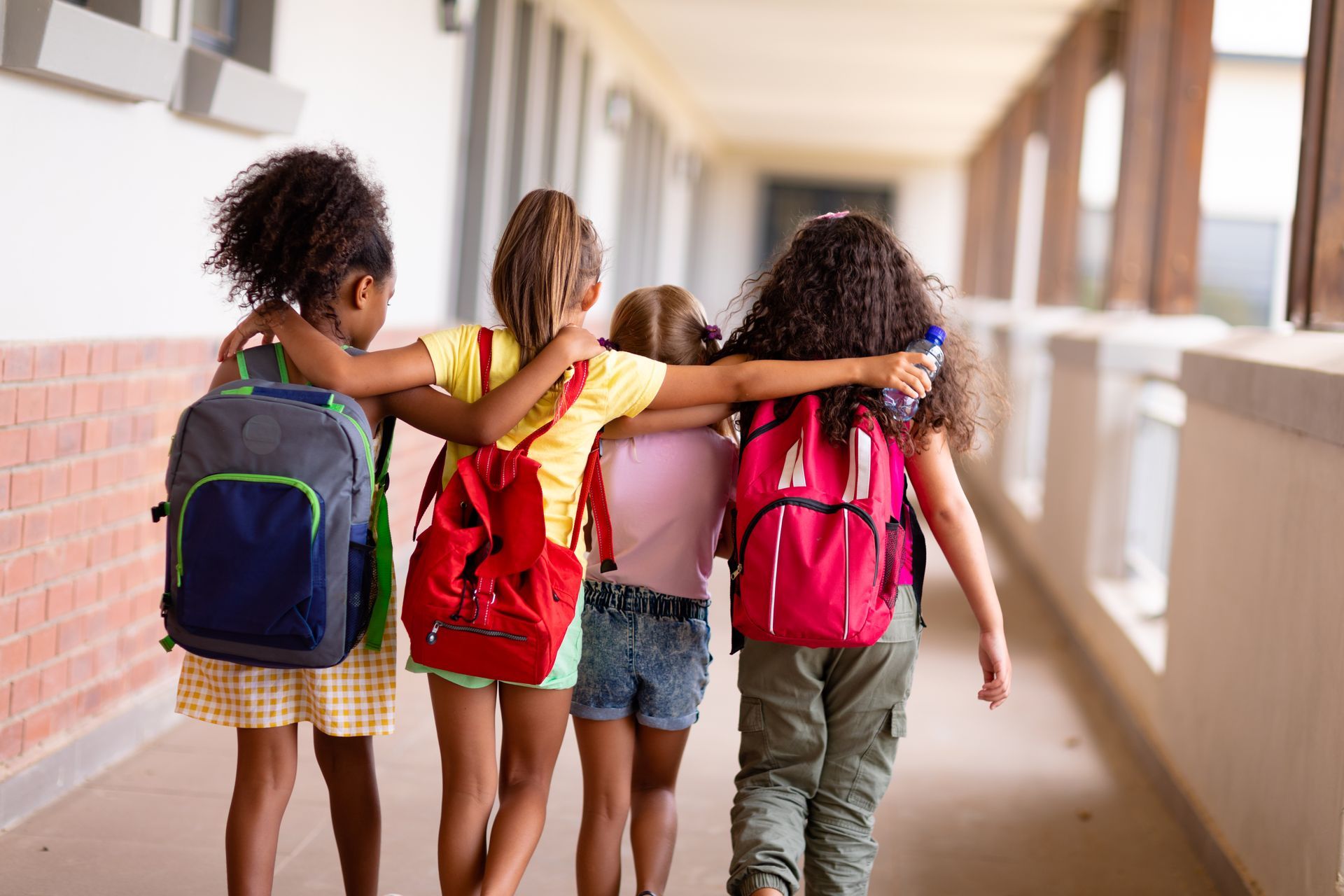 Three children with backpacks walking arm-in-arm down a school hallway