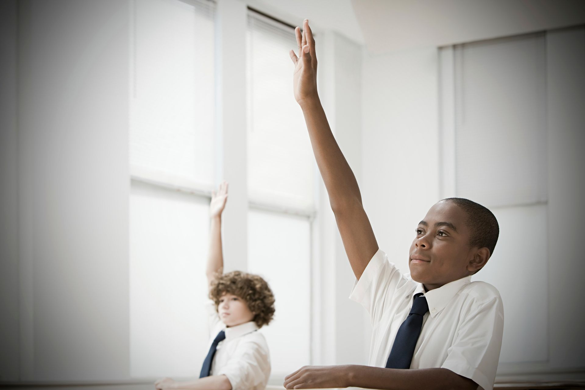 private school boys in a uniform raising their hand in class.