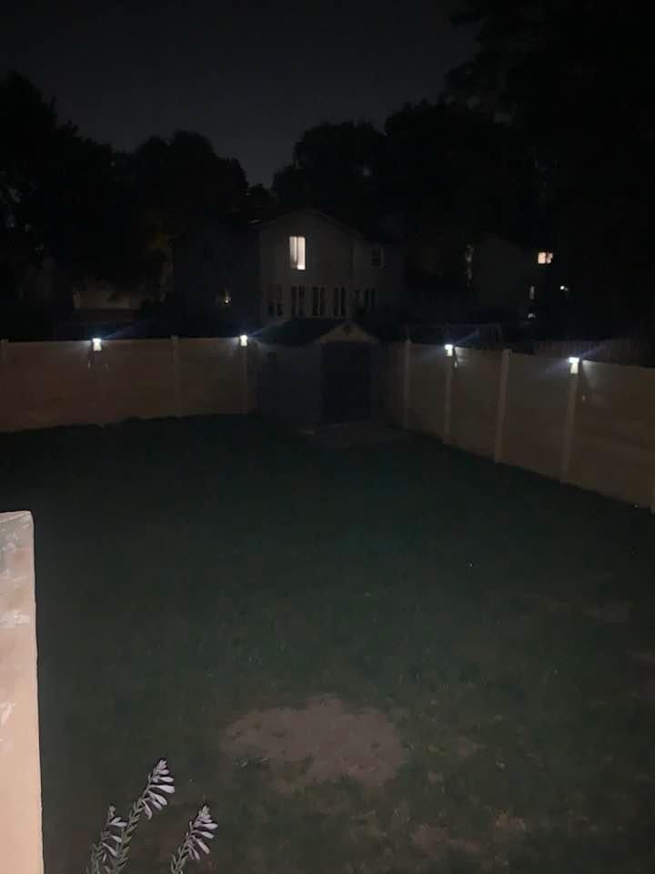 A dark backyard with a fence and a house in the background at night.