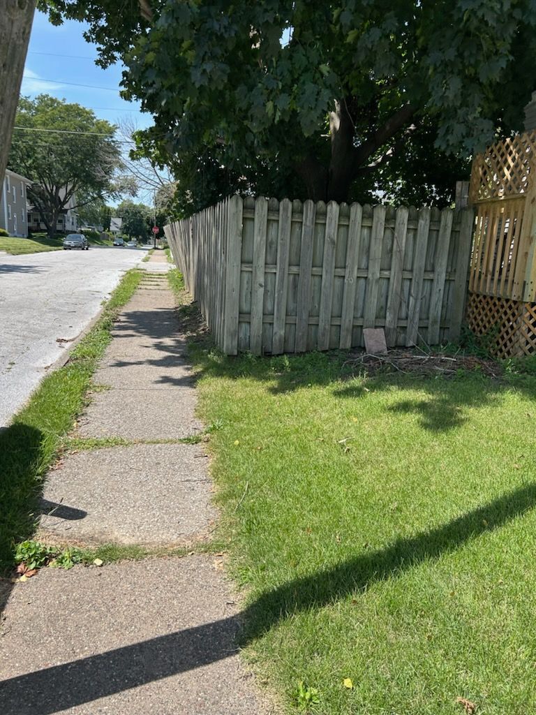 A wooden fence surrounds a sidewalk in a residential neighborhood.