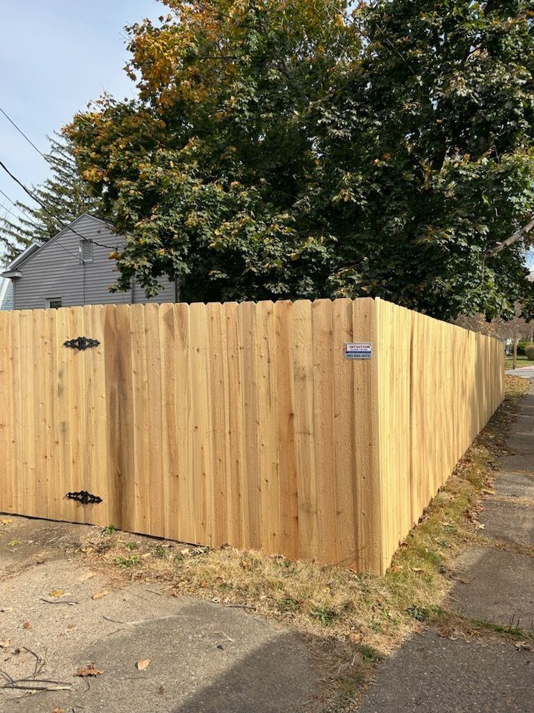 A wooden fence next to a sidewalk and to a house.