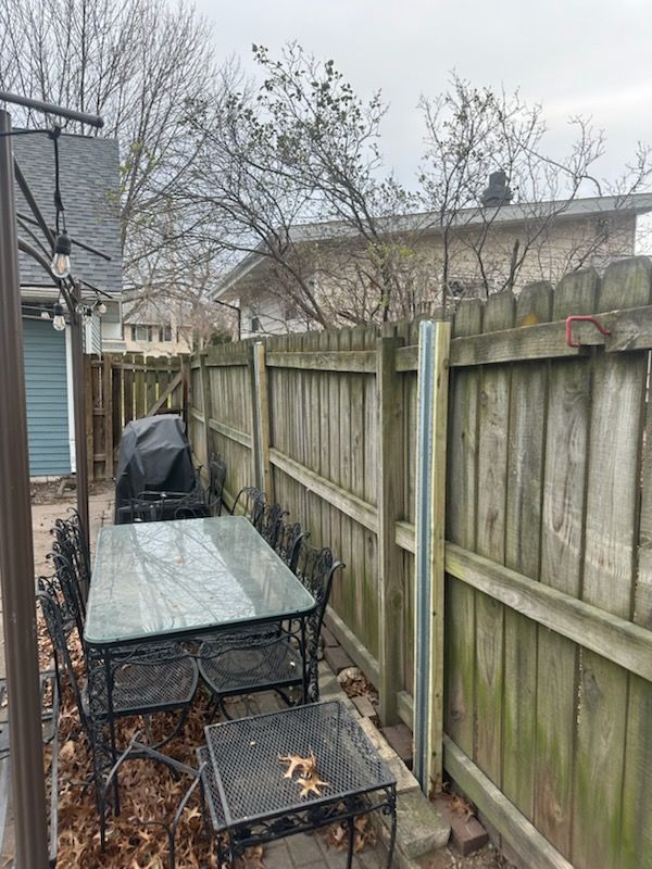 There is a table and chairs in the backyard next to a wooden fence.