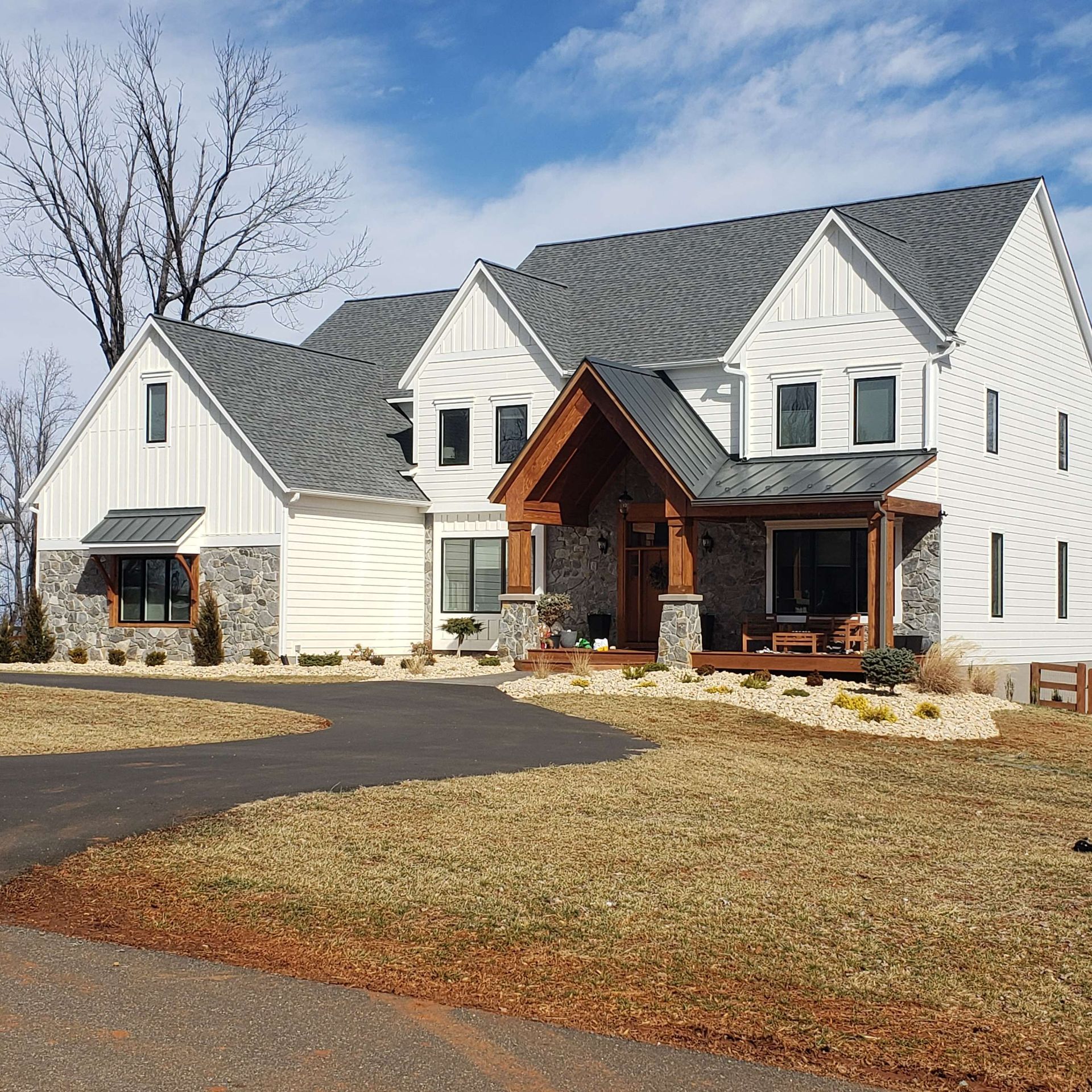 Large white two-story house with gray roof, stone-and-wood front entry, and bare yard under a clear sky