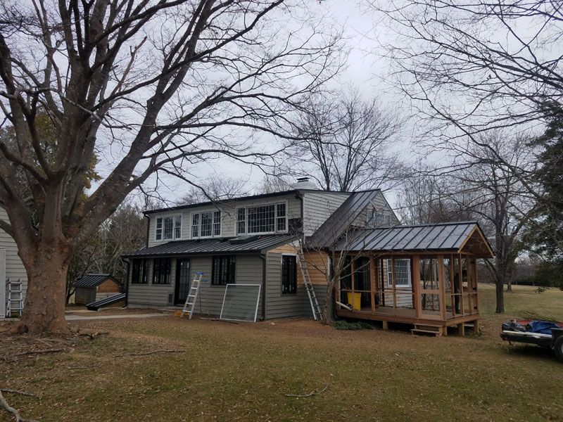 Old two-story house with a porch and attached glass greenhouse in a leafless yard