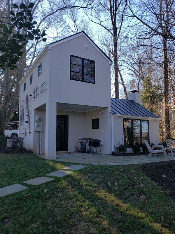 Two-story white house with dark roof and porch, set in a wooded yard at dusk.