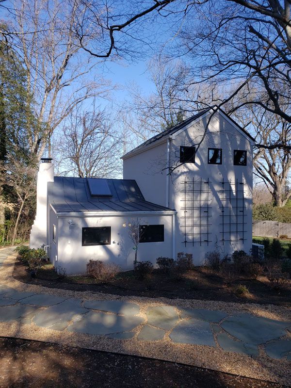 White house with attached garage and bare trees in a wooded yard on a sunny day