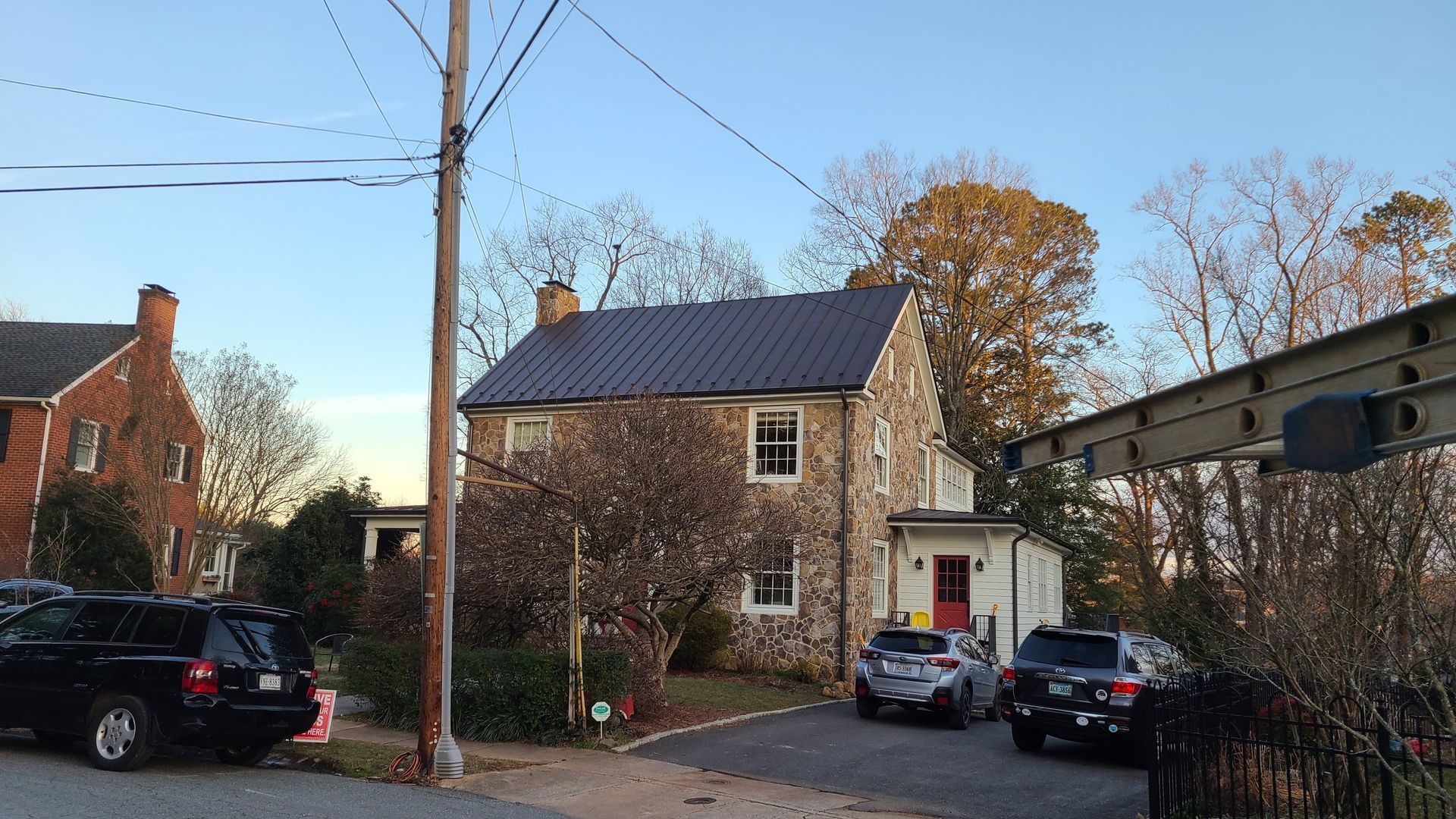 Stone house on a quiet residential street with parked cars and bare trees at dusk