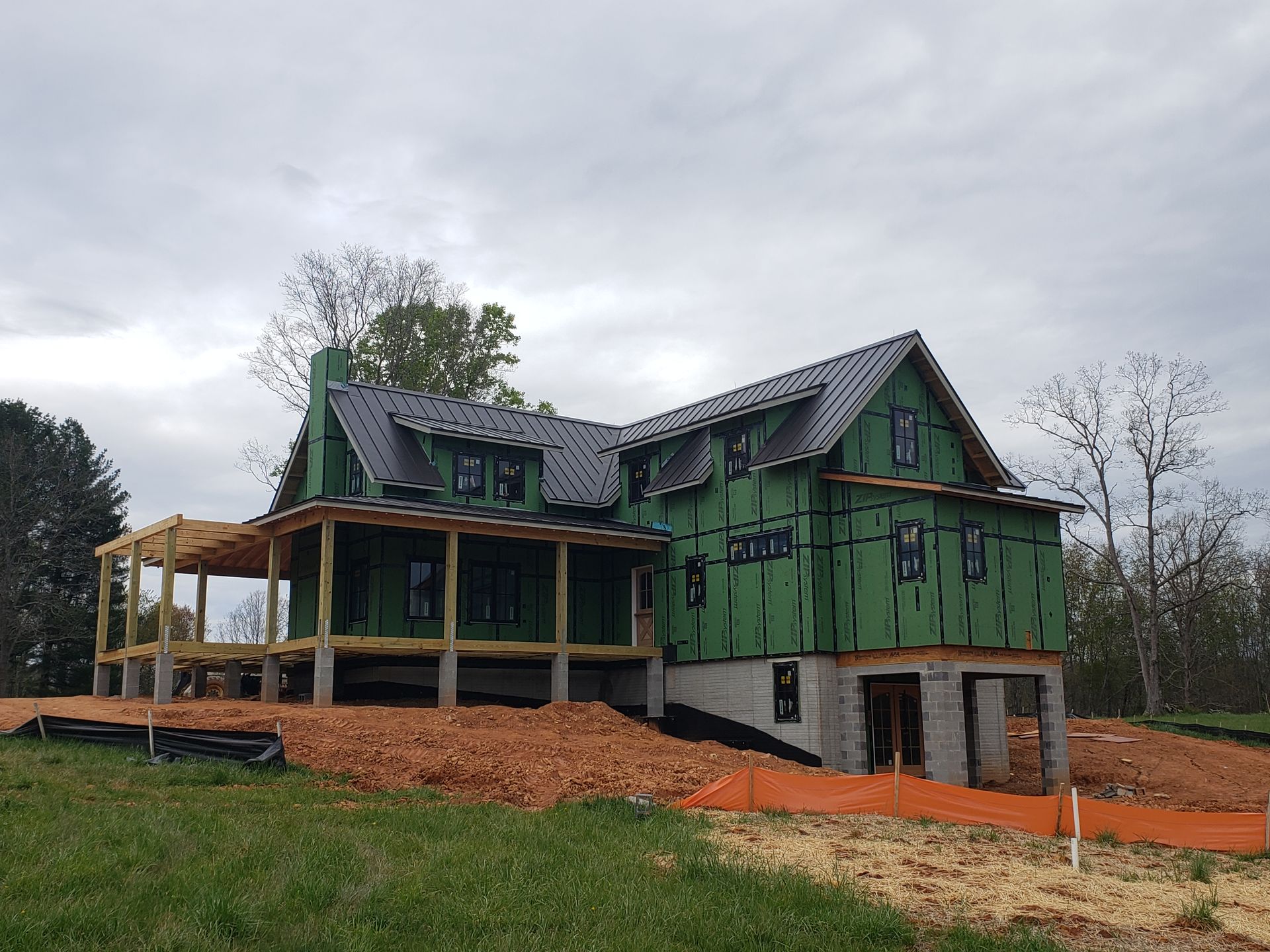Green house under construction with unfinished porch and exposed framing on a cloudy day