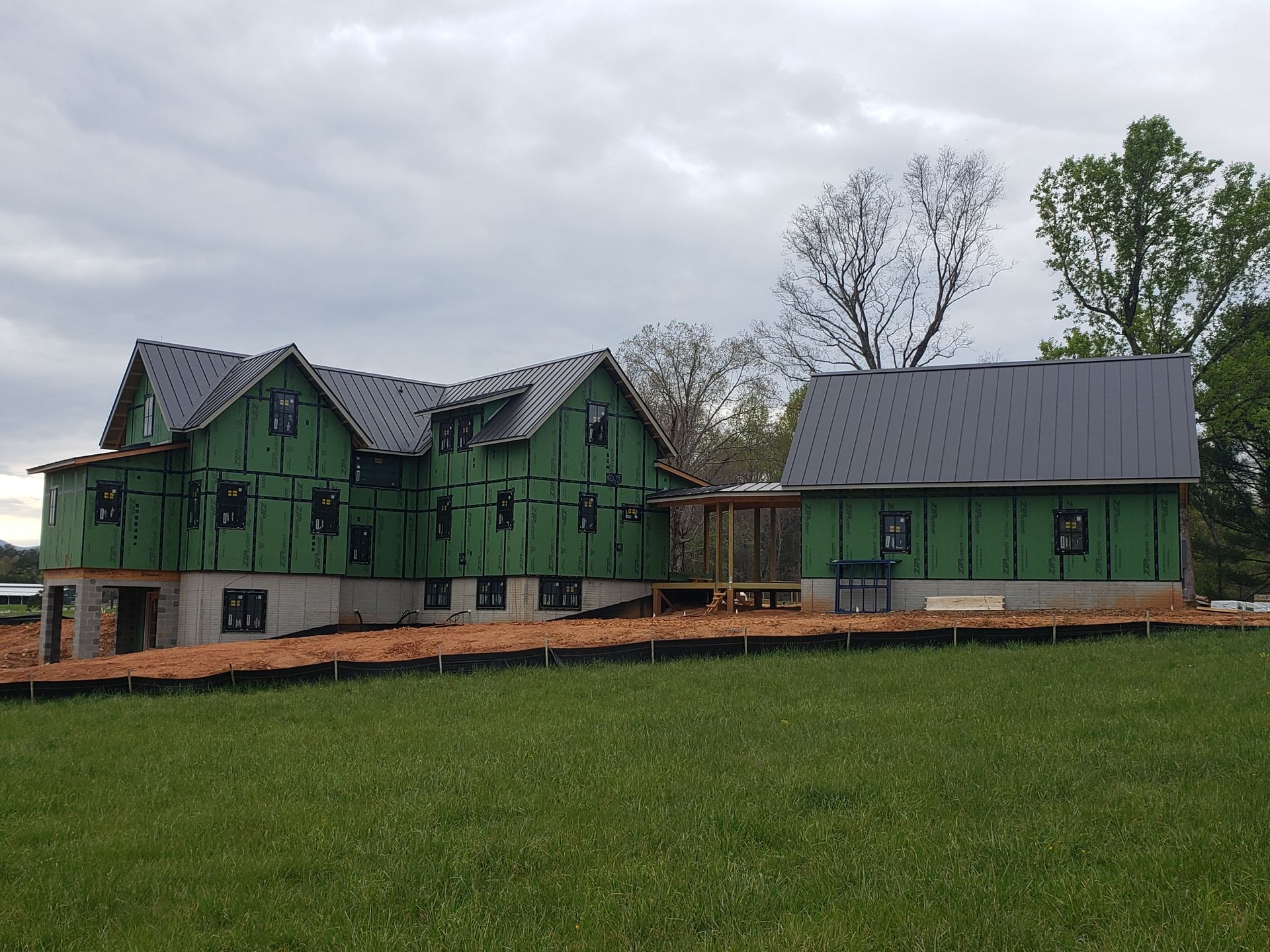 Green house under construction with scaffolding, on a grassy lot beneath a cloudy sky
