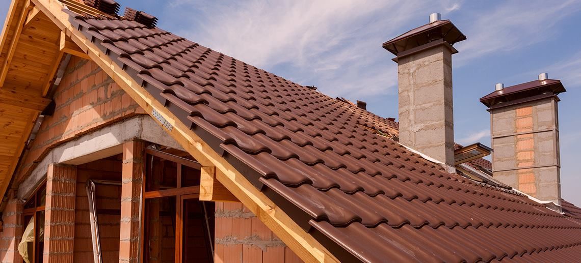Red-tiled roof with two brick chimneys on a house under a blue sky
