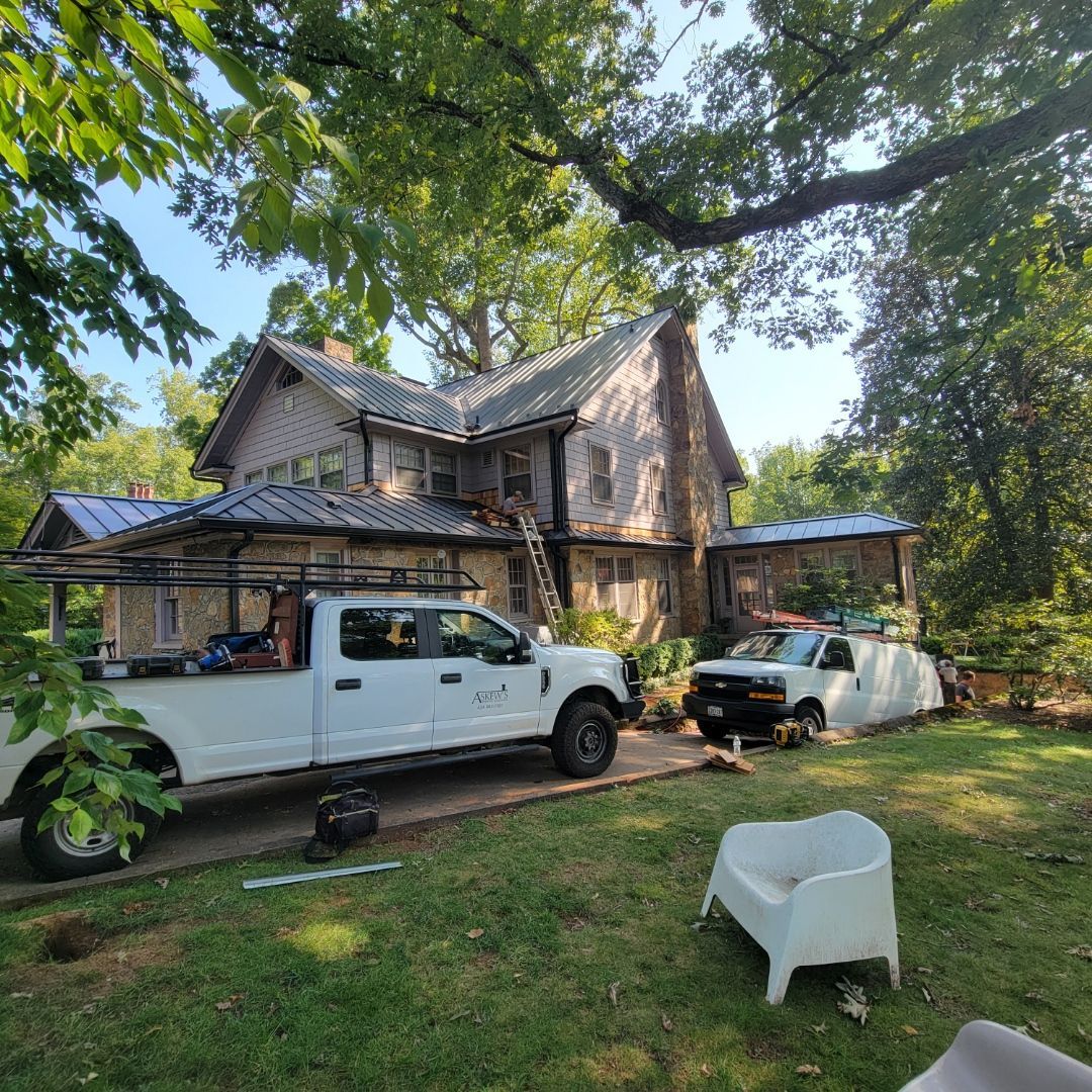 Two white work trucks parked in front of a rustic house in a wooded yard