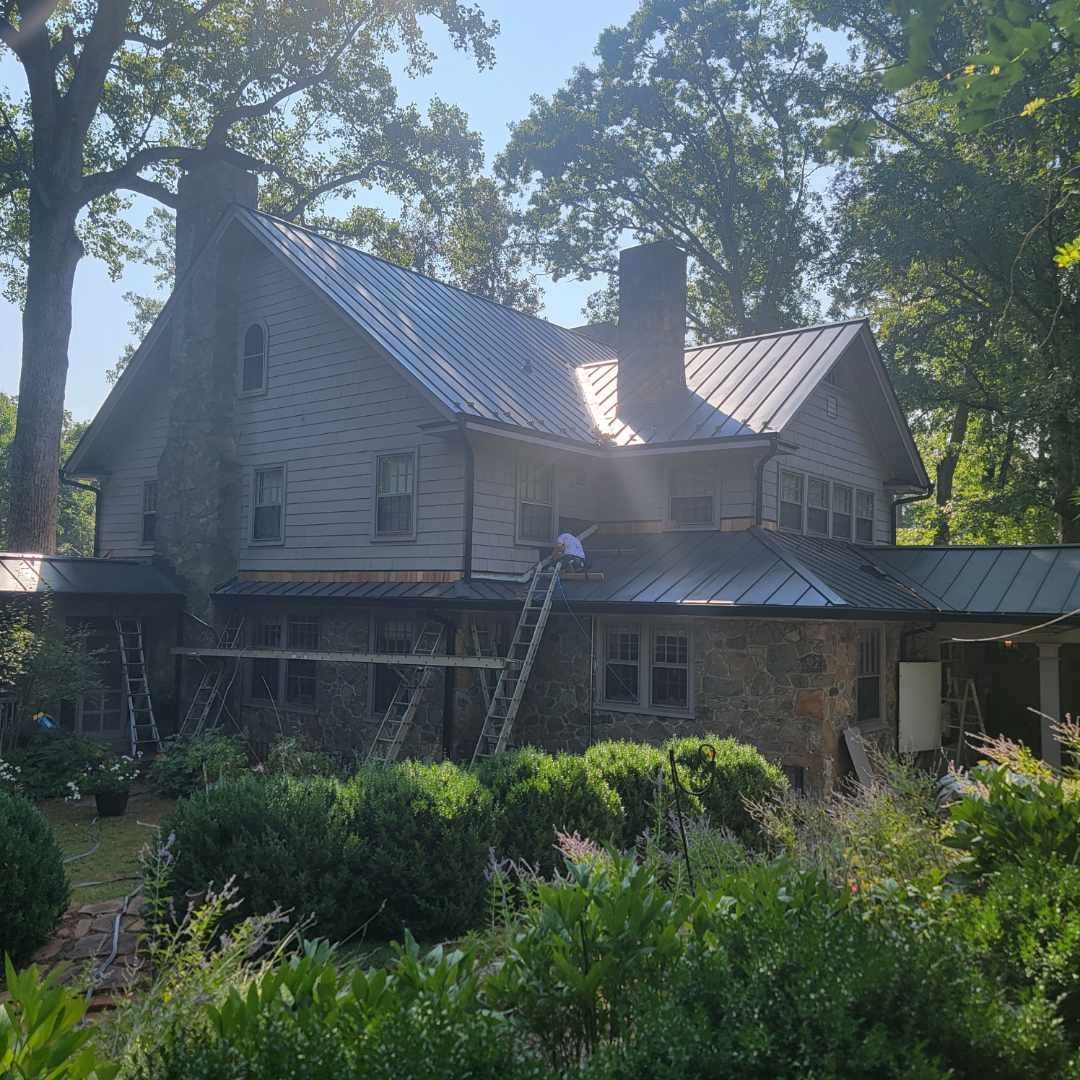 Stone house with metal roof amid dense green garden trees in bright sunlight