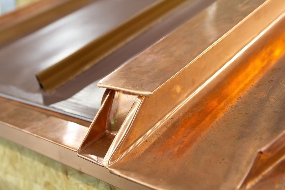 Close-up of copper metal roofing panels with raised seams and orange-brown reflections