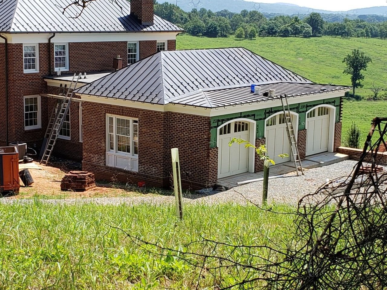 Brick garage with white doors beside a house, overlooking green fields and hills