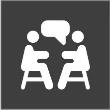 White icon on a dark gray square showing two people sitting and facing each other with a speech bubble above them.