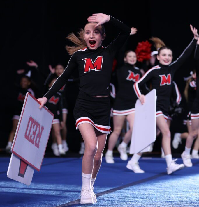 Two cheerleaders in black and red uniforms perform a mount, with one standing on the shoulders of the other.