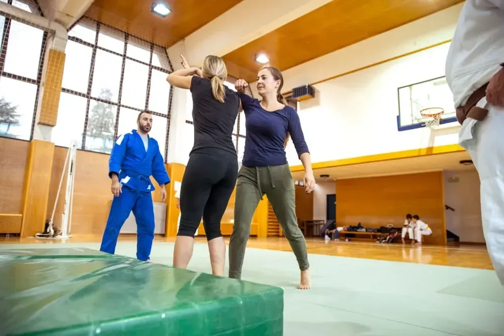 Two people practicing a lift in a gymnasium while a coach watches nearby