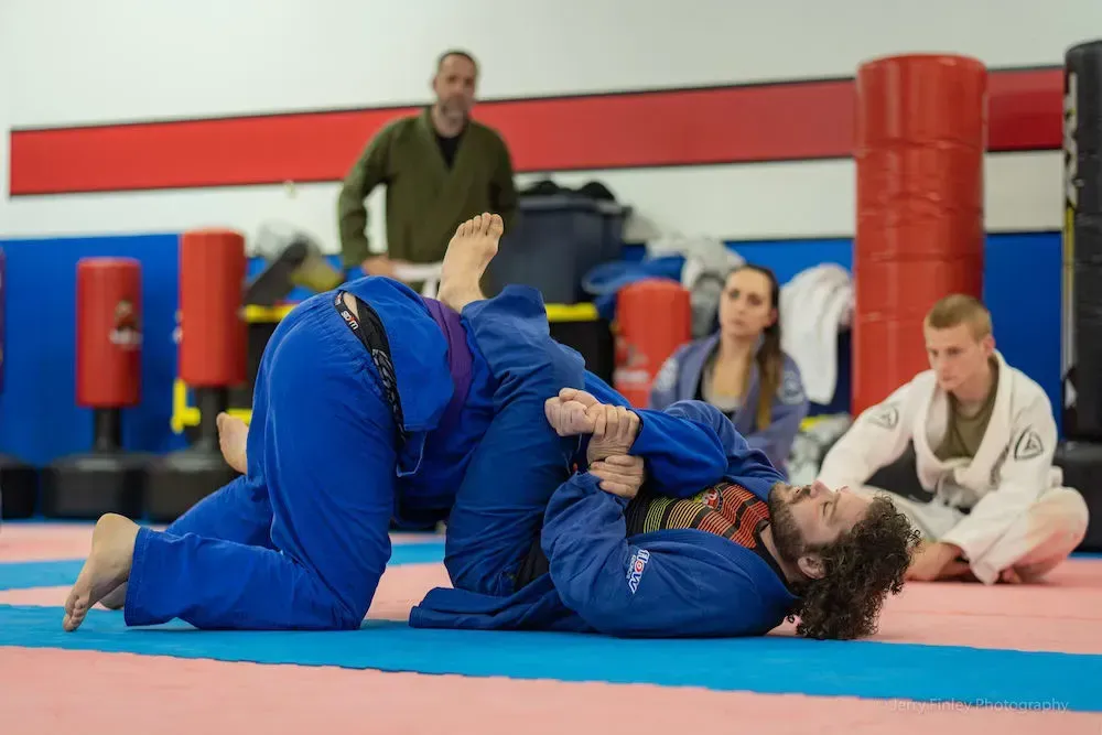 Two judo athletes in white gis grappling on a blue mat in a gym