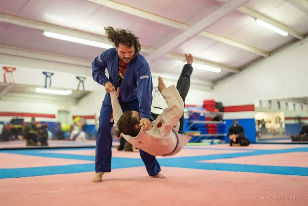 Two people grappling on a gym mat while two others watch from the background