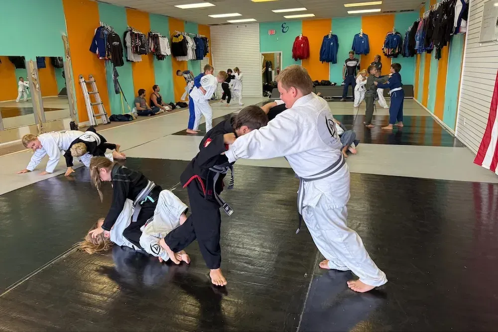 Two judo practitioners in white uniforms with black belts standing on a yellow mat
