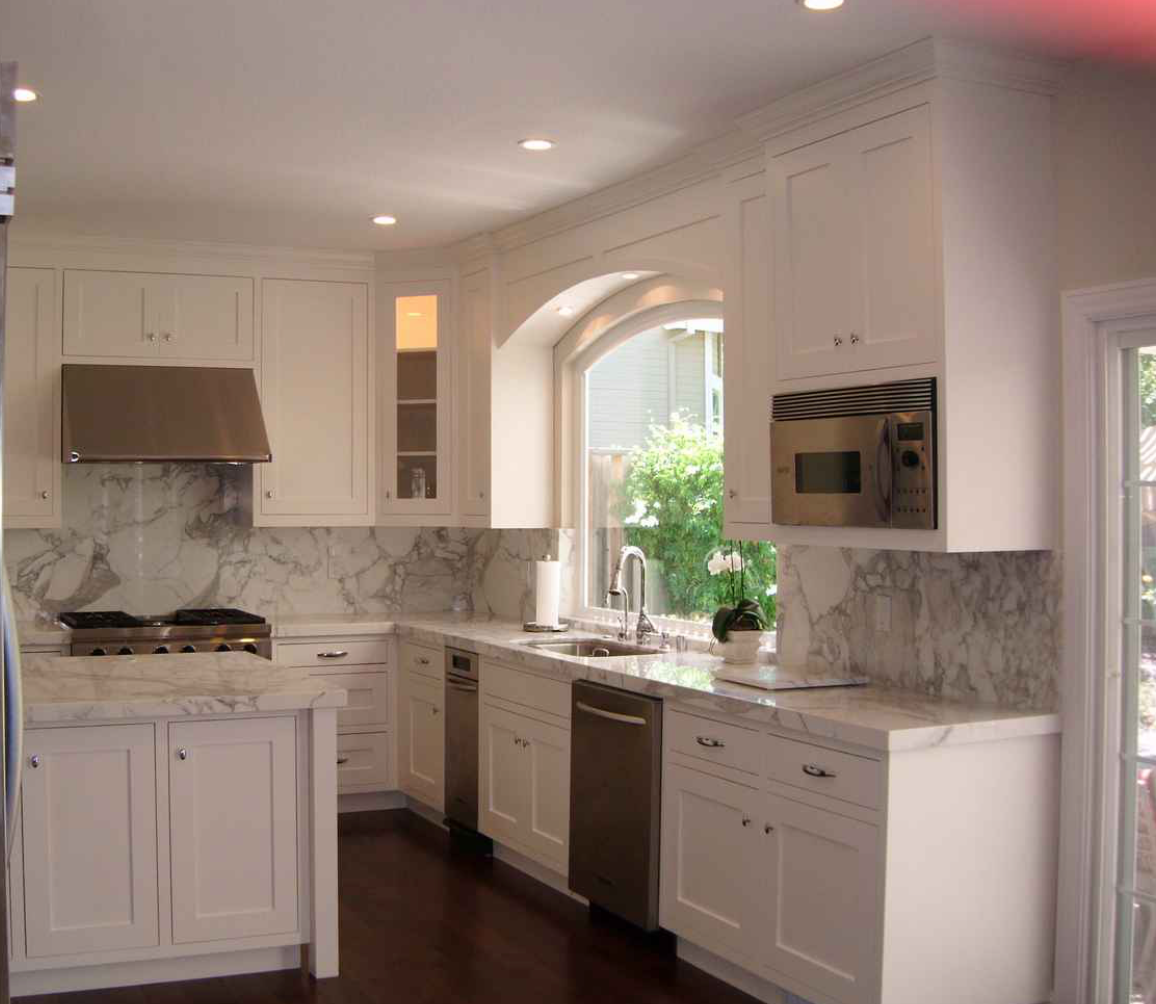 White kitchen with marble countertops and cabinets, stainless steel appliances, and dark hardwood floors.