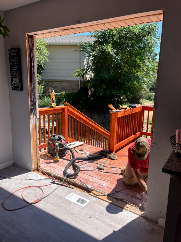 A person working on a deck, visible through a doorway. Construction materials and tools are present.