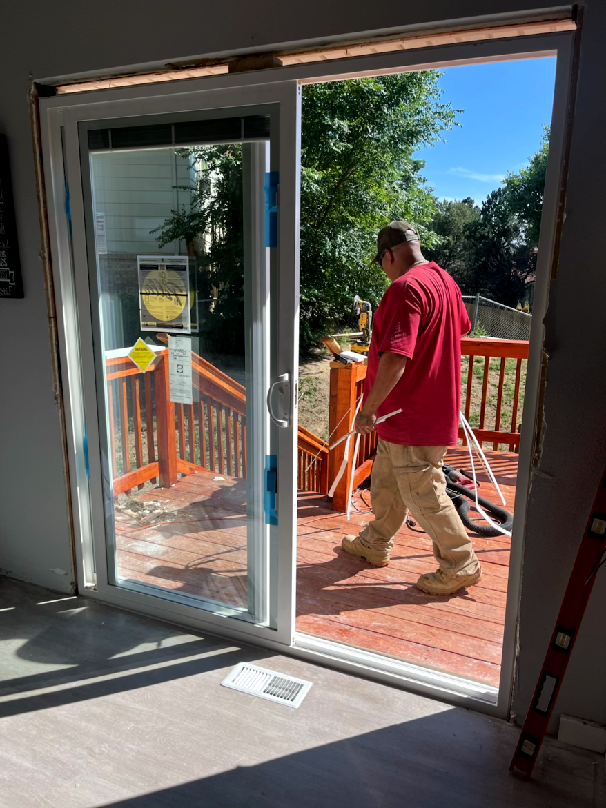 A person walks through a newly installed sliding glass door onto a wooden deck; interior and exterior views.