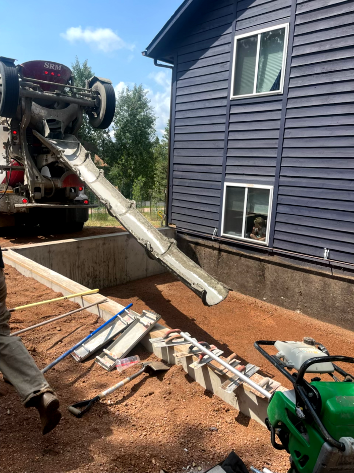 Concrete being poured into a foundation next to a blue house by a cement truck.