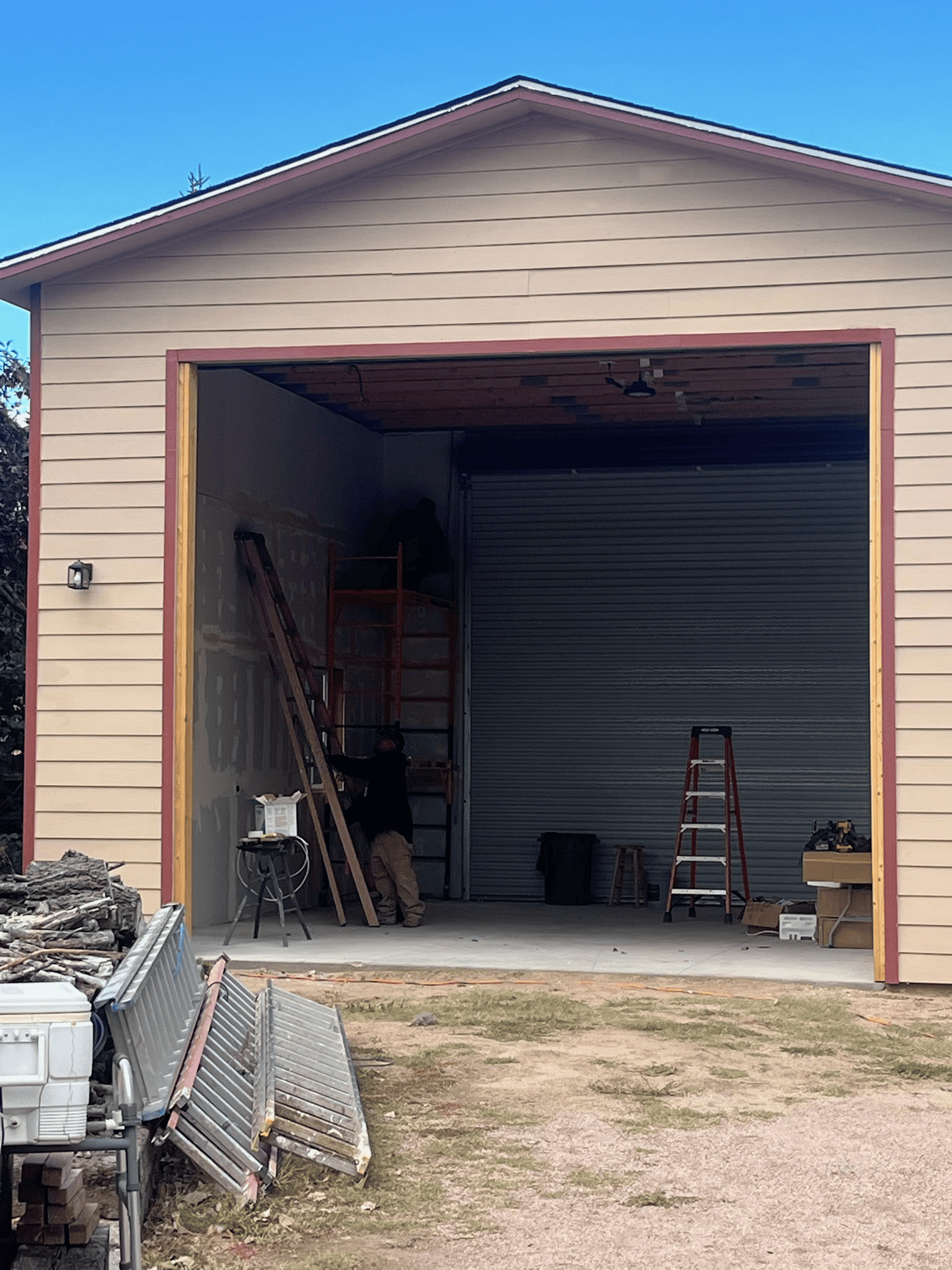Garage with open door, person on ladder. Beige siding, red trim. Exterior shot.