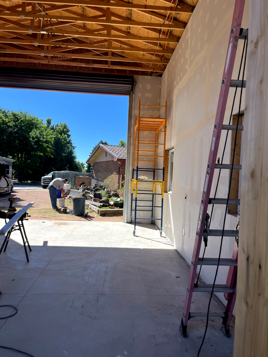 Construction site: Open doorway reveals a man working outside. Ladder leans against the stucco wall.
