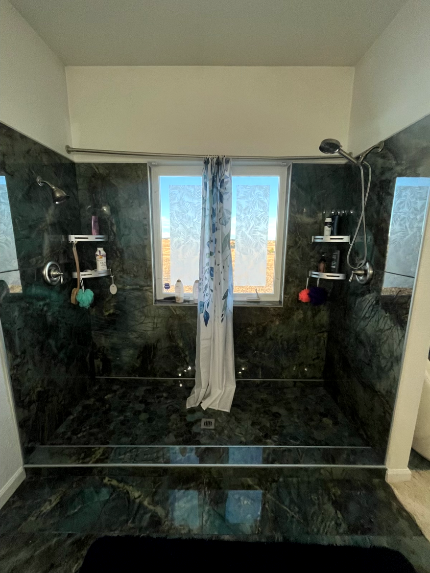 Dual shower with dark green marble walls, a window, and showerheads.