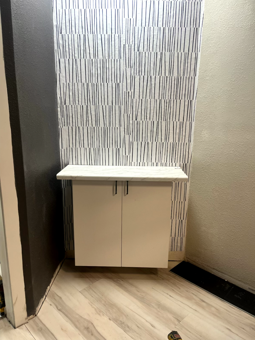 White wall-mounted cabinet with two doors, on a white and black striped wall.