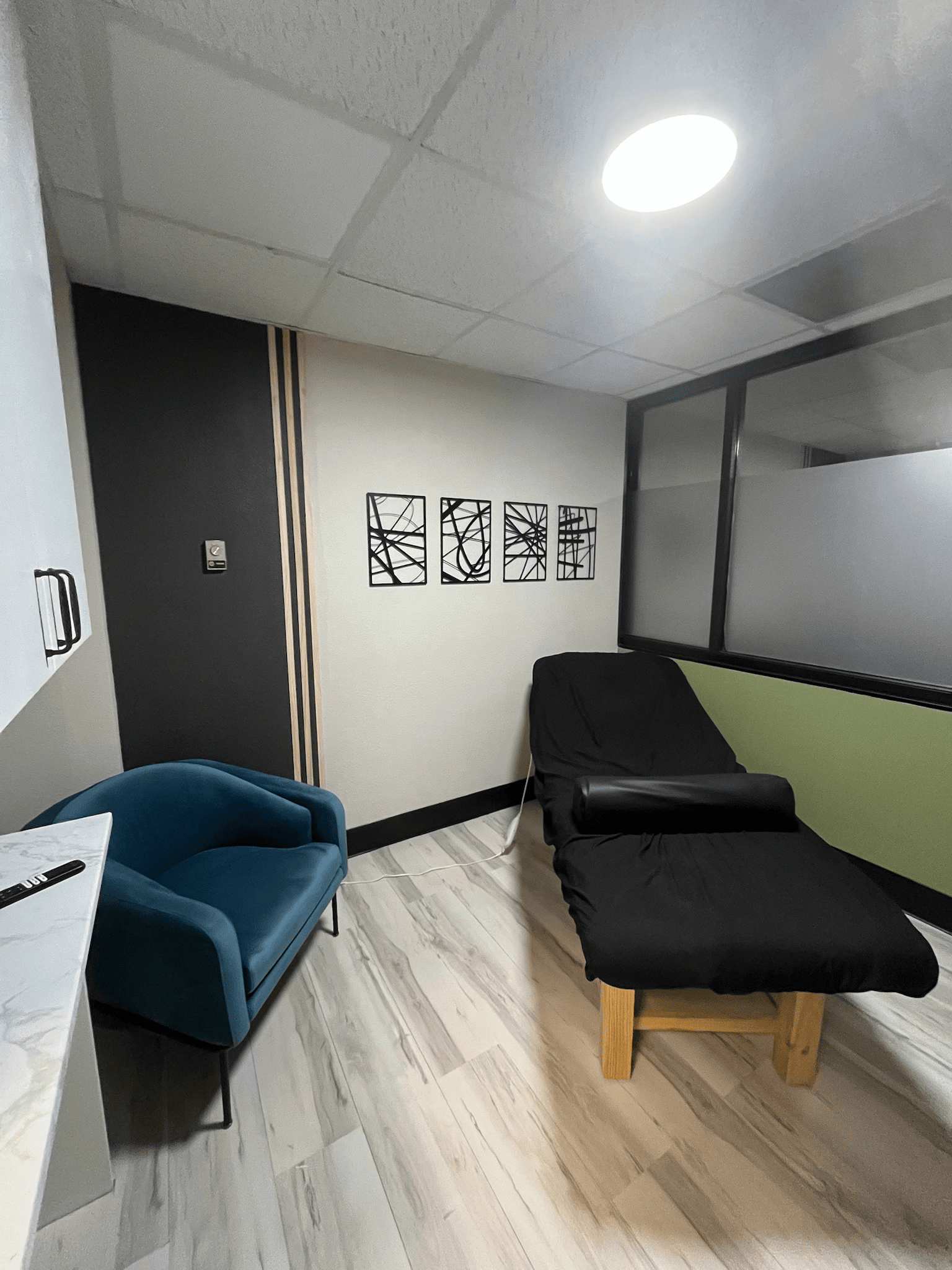 Small massage room with blue chair, black massage table, and decorative wall art.
