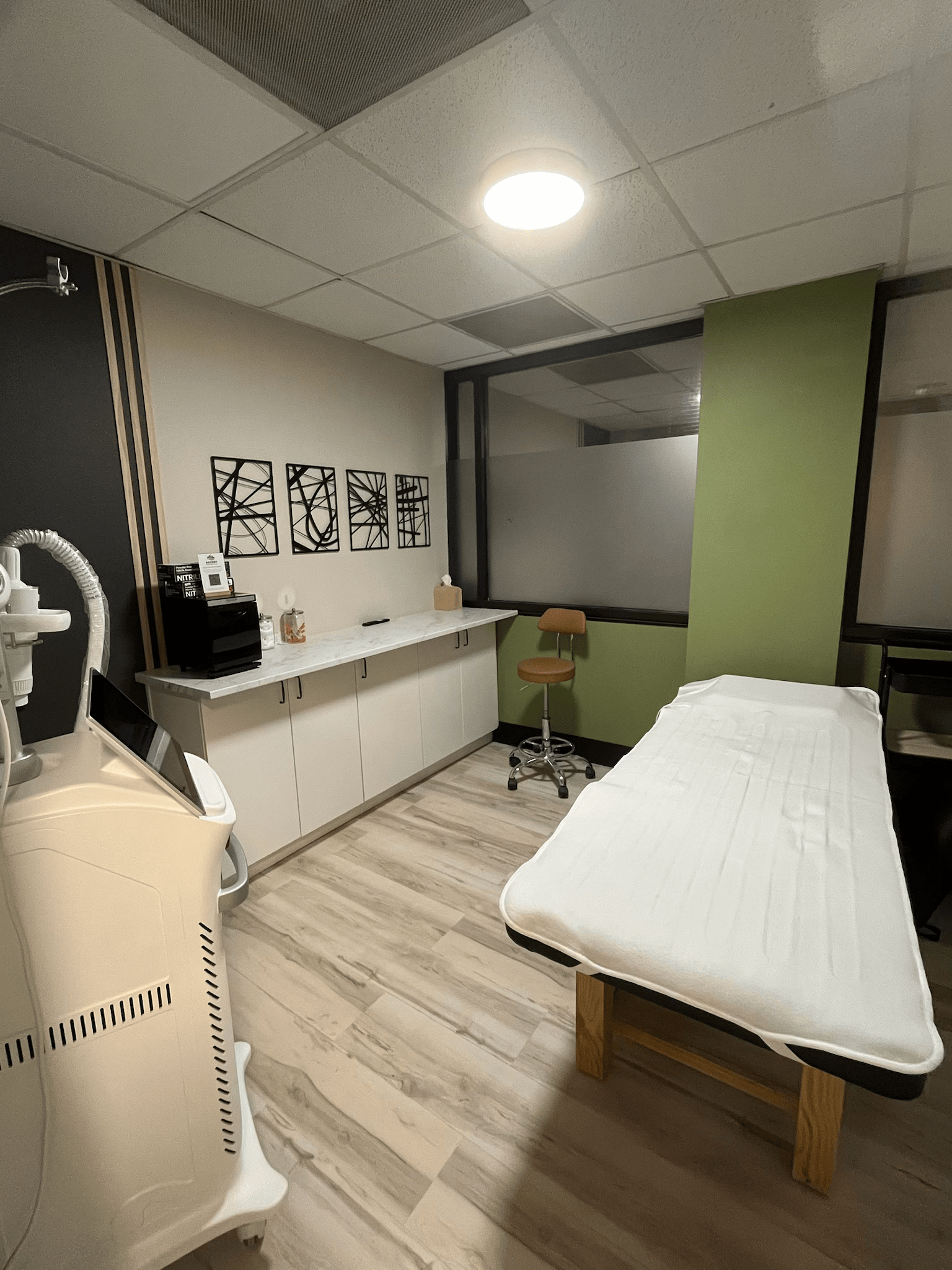 Treatment room with massage table, medical equipment, desk, and chair.