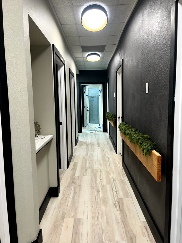Long hallway with gray and black walls, wood-look floor, doors, and three ceiling lights.
