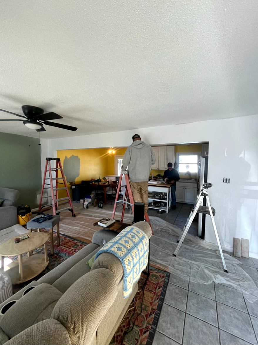 People painting a room during a home renovation, with ladders and covering the floor.
