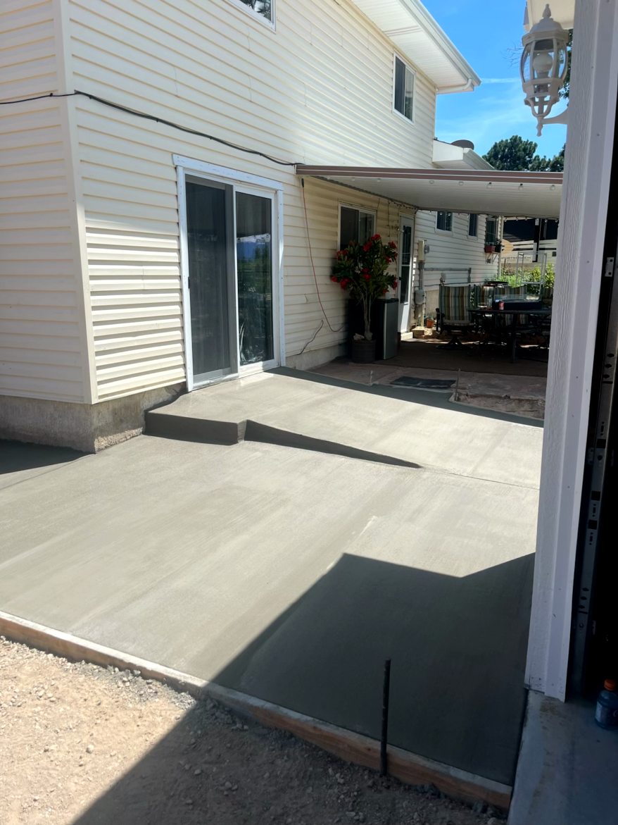 Newly poured concrete patio next to a house with a sliding glass door and covered area.