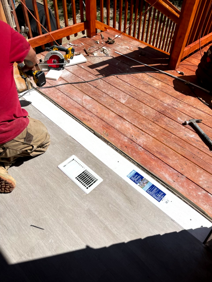 Person installing gray flooring on a deck. A circular saw and vent are visible.