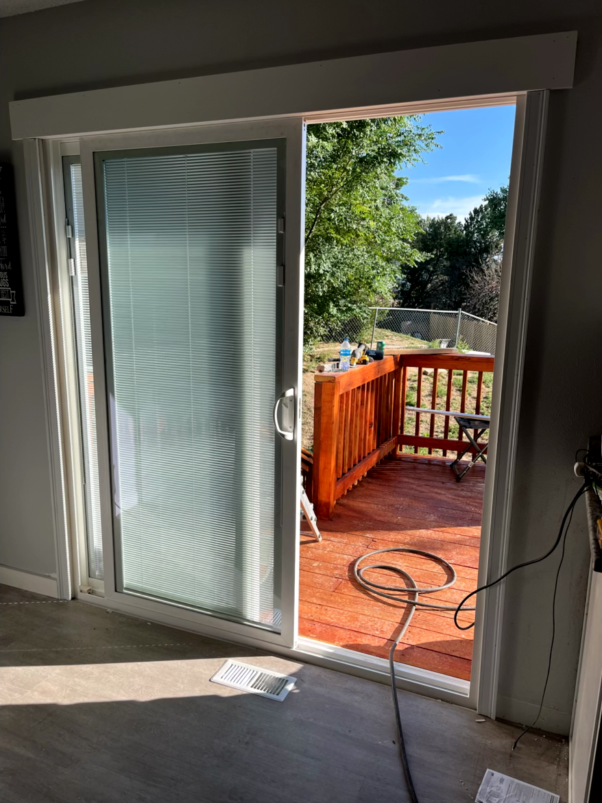 Sliding glass door open to a wooden deck. The frosted door is closed. Sunshine and greenery are visible.