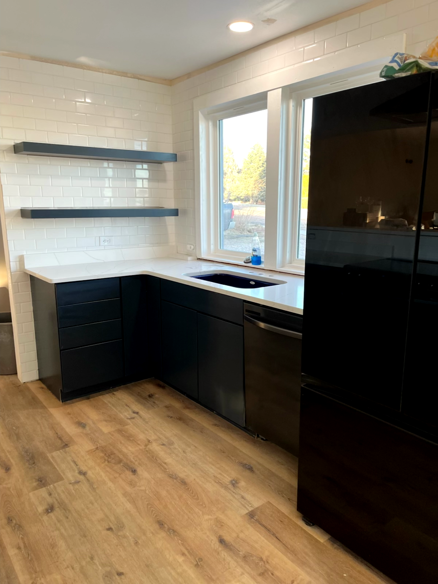 Modern kitchen with navy cabinets, white countertops, subway tile, and wood-look flooring.