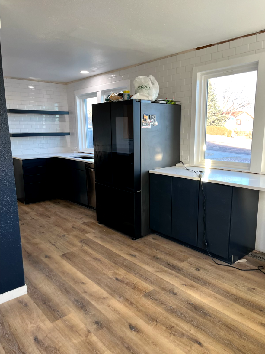 Modern kitchen with dark blue cabinets, stainless steel appliances, and wood-look flooring.