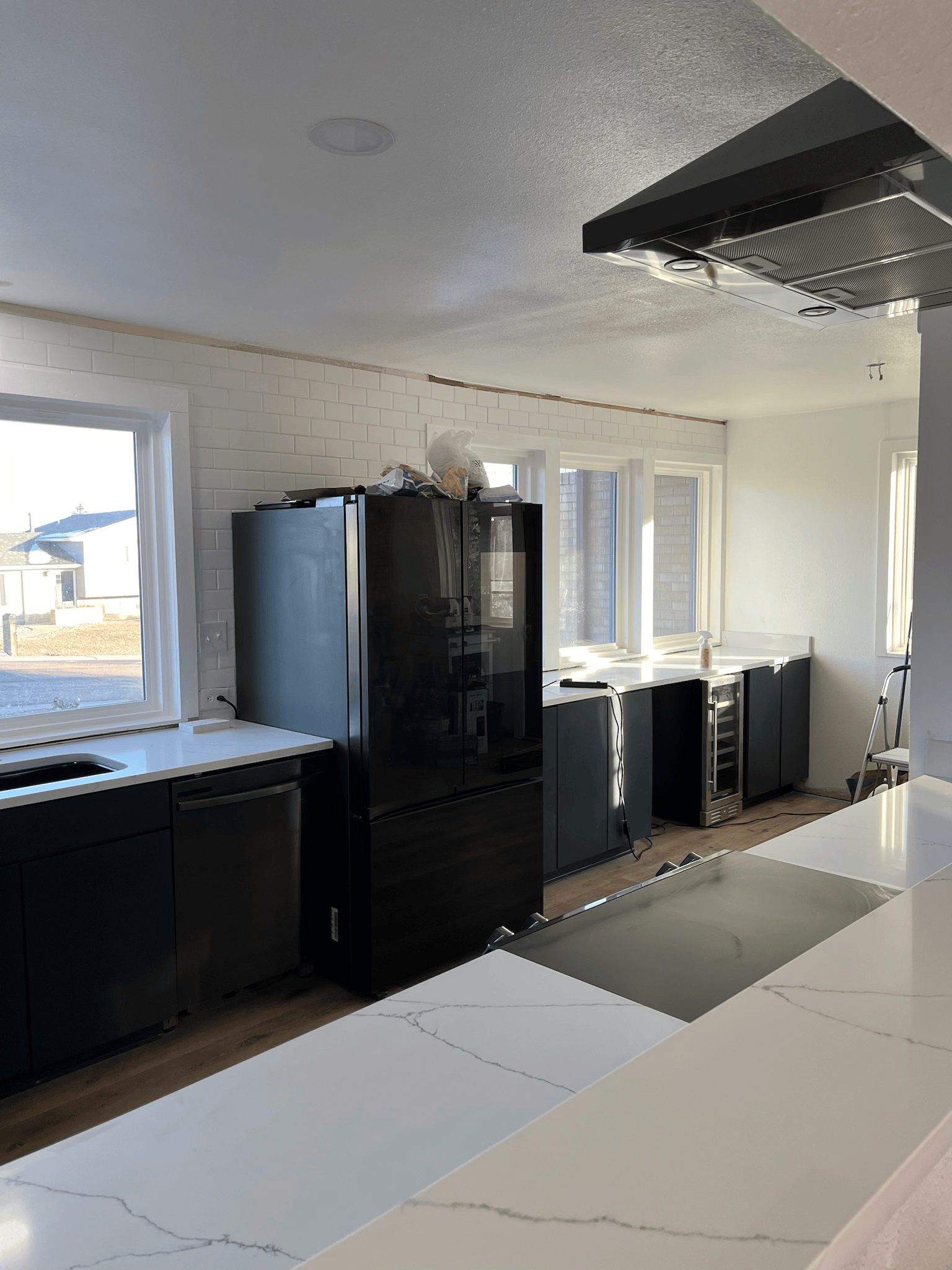 Modern kitchen with black cabinets, white countertops, and brick wall.