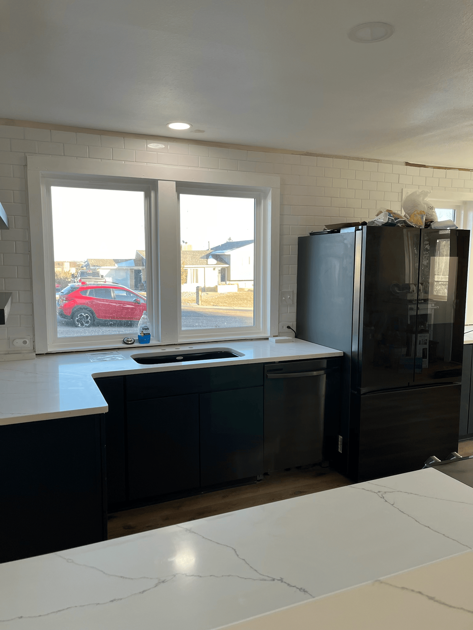 Kitchen with black cabinets, white countertops, window, and black refrigerator.