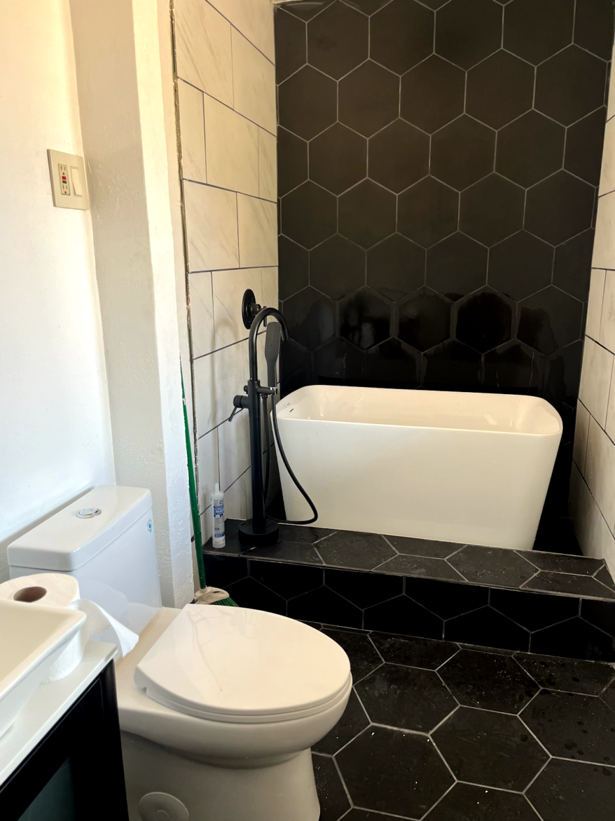 Bathroom with black hexagon tiles, white freestanding tub, and a toilet.