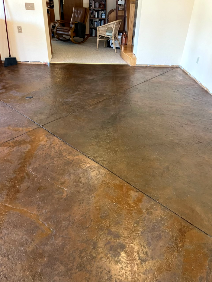 Brown stained concrete floor, with dark lines, leads into a room with furniture.