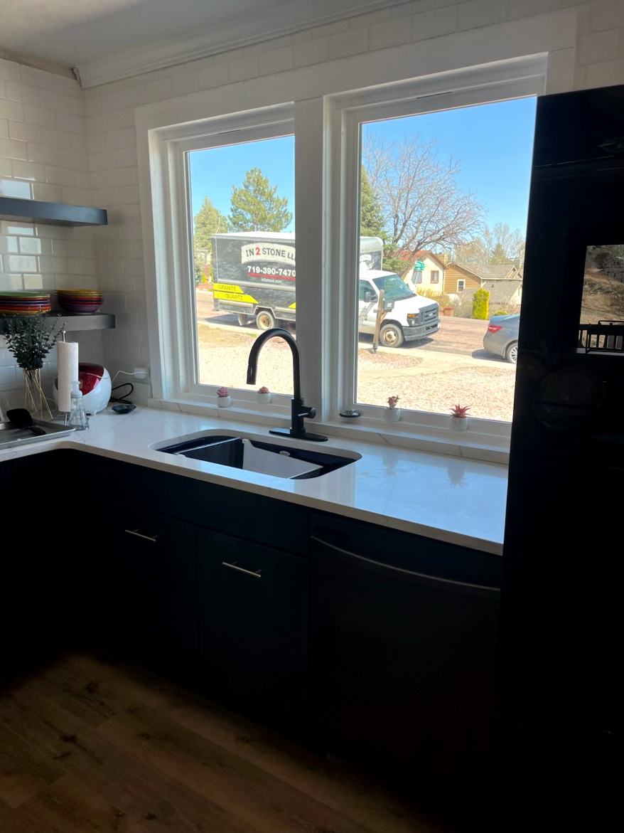 Kitchen with white countertops, black cabinets, and a sink beneath a window overlooking a street with vehicles.