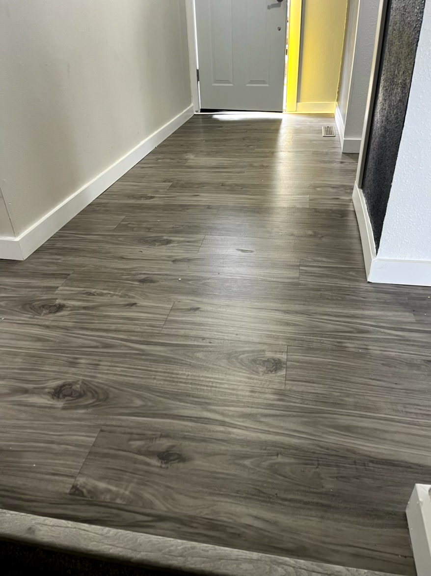Gray wood-look flooring extends down a hallway, leading to a white door. White trim lines the walls.