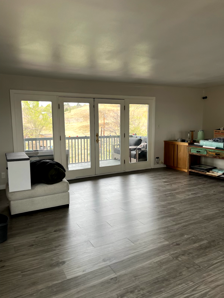Empty living room with French doors leading to a balcony. Gray floor, wooden cabinet, white walls.